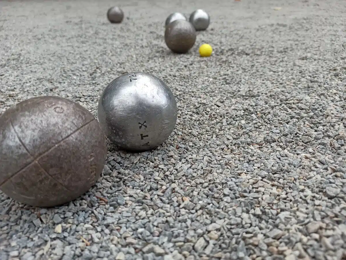 Les règles de la Pétanque : le guide complet et à jour 2 Deux boules de Pétanque au premier plan, le cochonnet jaune et d'autres boules plus loin sur un terrain en gravier