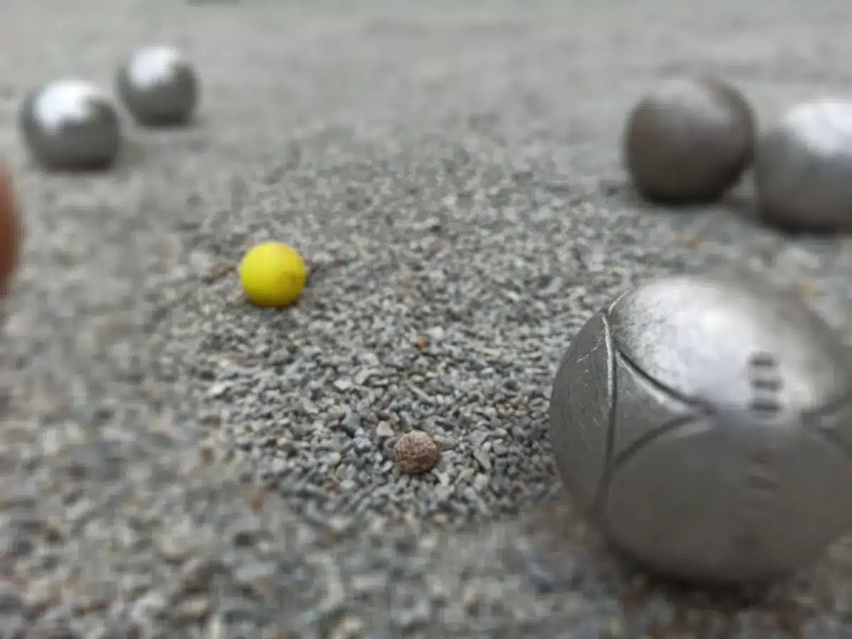Pourquoi marquer le cochonnet à la Pétanque ? La règle et les bons gestes 1 Cochonnet jaune posé sur le gravier, à quelques centimètres d'une boule de Pétanque