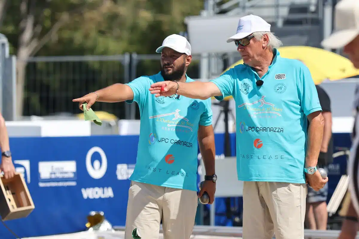 How to progress in petanque: training, technique and the mental game 3 Two teammates in turquoise polo shirts gesturing towards the boule to play on a competition terrain