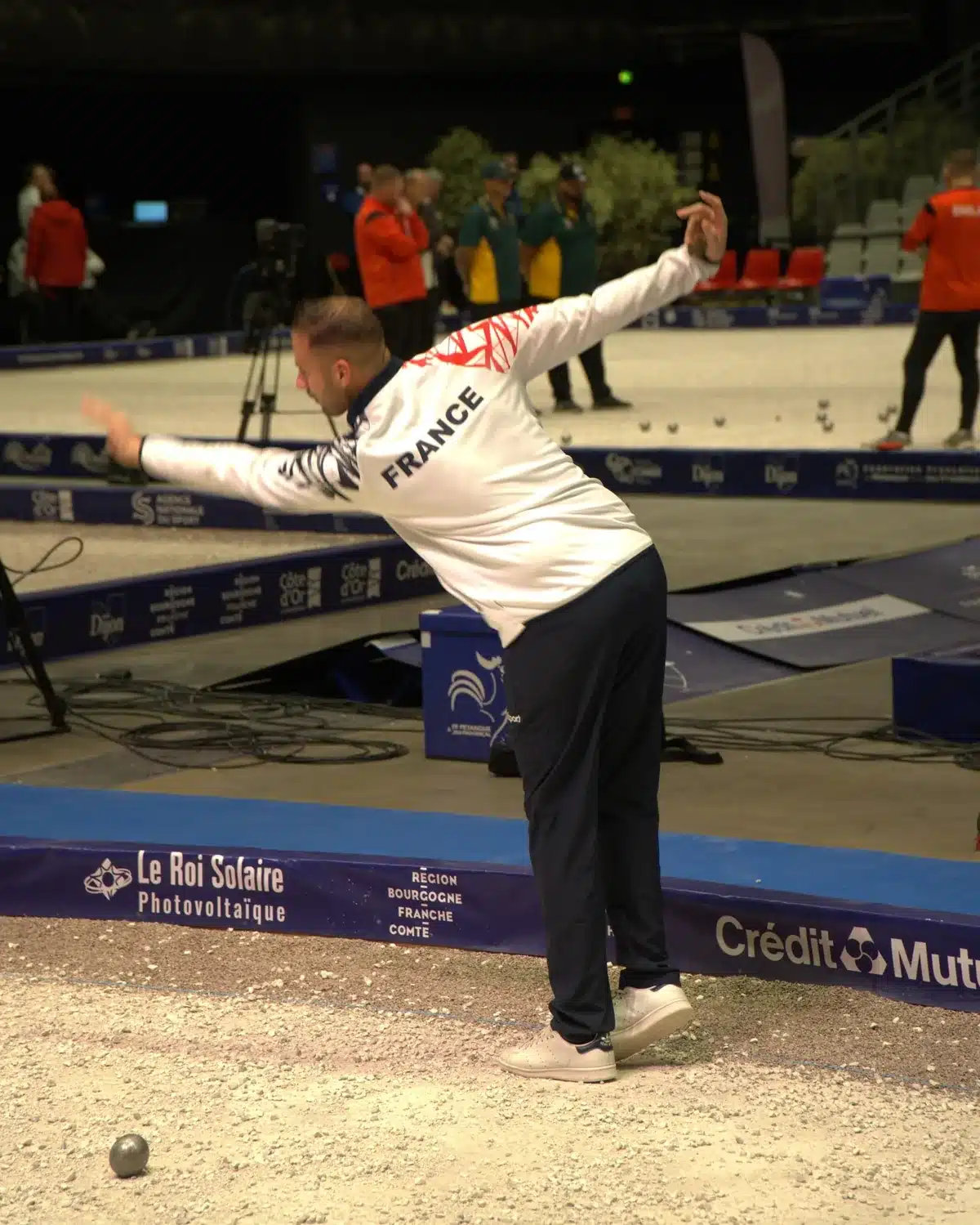 Precision shooting in petanque: rules, 5 workshops and practice 11 Dylan Rocher, in a white France team jacket, arms outstretched just after the release of his boule, in a competition hall