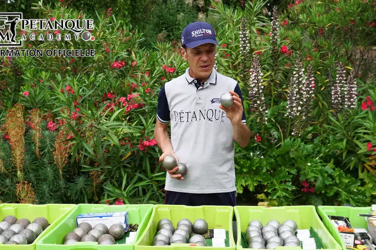 Choisir ses boules de Pétanque : tableau des diamètres, poids et dureté 1 Jean-François tient des boules de Pétanque devant des bacs remplis de jeux de différents modèles