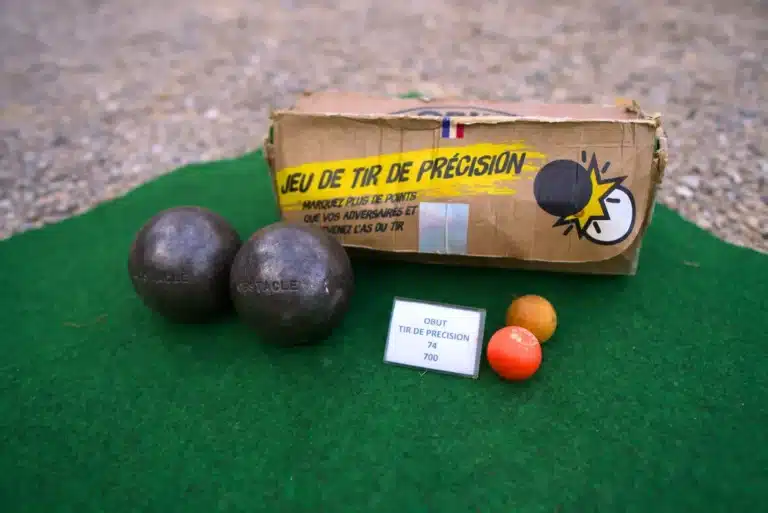 Jeu de tir de précision Obut : deux boules obstacles noires, deux buts et le carton du kit posés sur un tapis vert