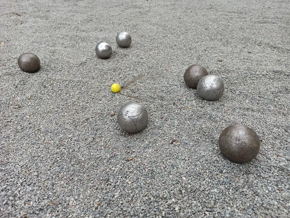 Pourquoi marquer le cochonnet à la Pétanque ? La règle et les bons gestes 3 Mène de Pétanque vue d'en haut : le cochonnet jaune entouré de boules sur un terrain en gravier