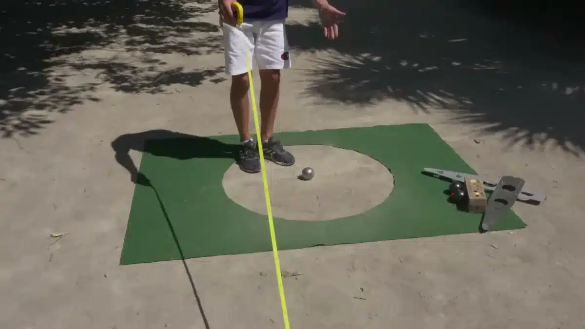 Precision shooting in petanque: rules, 5 workshops and practice 7 Yellow 10-metre tape stretched along the ground to the target circle mat, with the target boule in the centre and the template and obstacle boules laid beside it