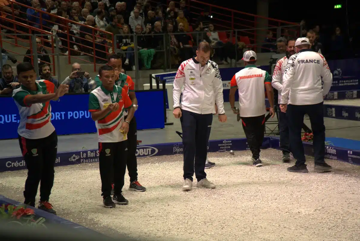 Les règles de la Pétanque : le guide complet et à jour 1 Partie de Pétanque en compétition dans une salle : un joueur lance sa boule, coéquipiers et adversaires attendent derrière lui