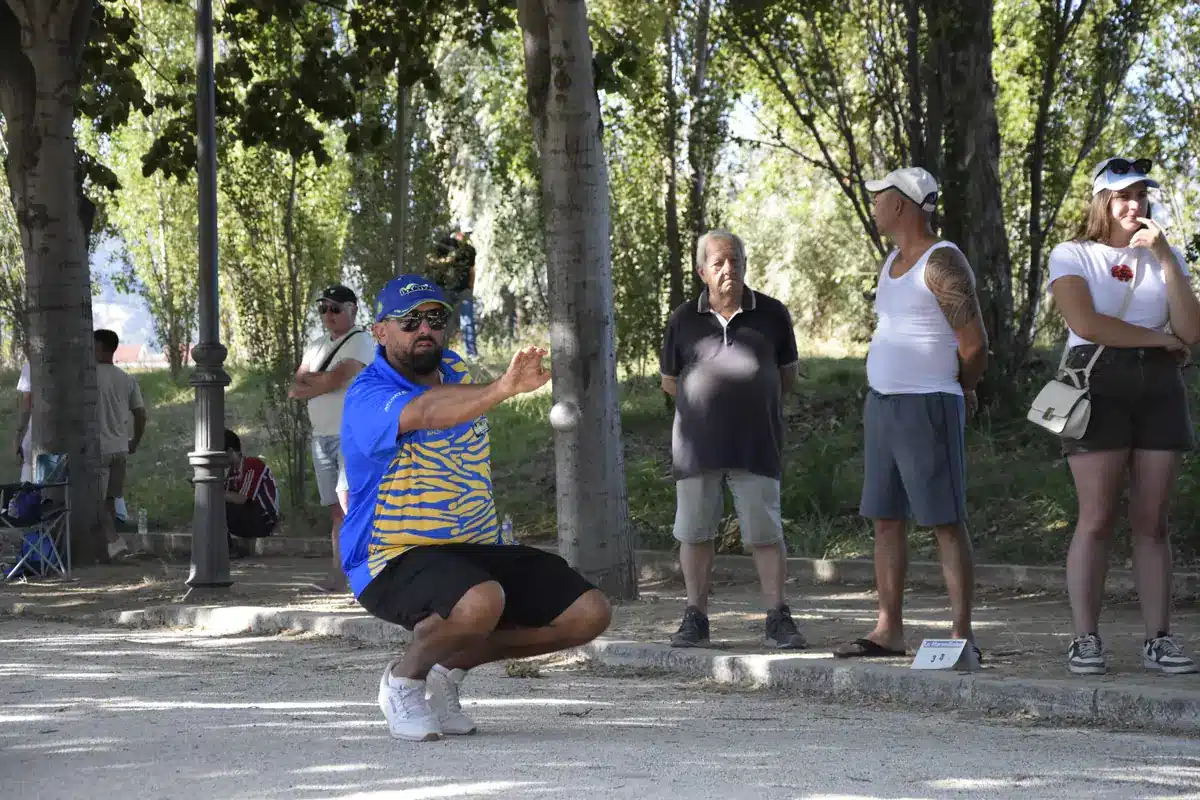 How to progress in petanque: training, technique and the mental game 1 Crouching player who has just released his boule to point on a shaded terrain, in front of spectators