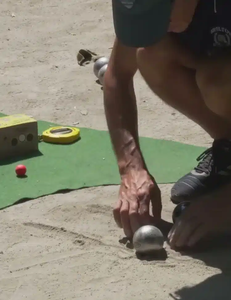 Precision shooting in petanque: rules, 5 workshops and practice 10 Hand putting the target boule back in the centre of the target circle mat, next to a red jack and a 10-metre tape